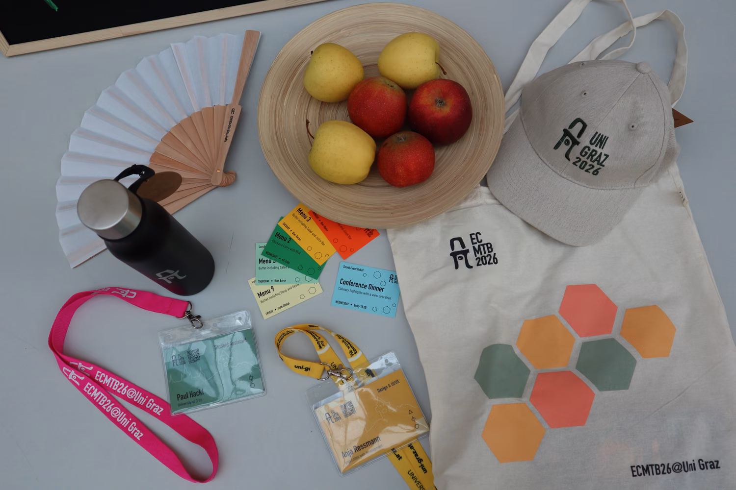 All items that were featured in the participant's goodie bag laid out on a table: the fan, a black waterbottle, a cap, the branded tote bag, lunch tickets, and the nametag.